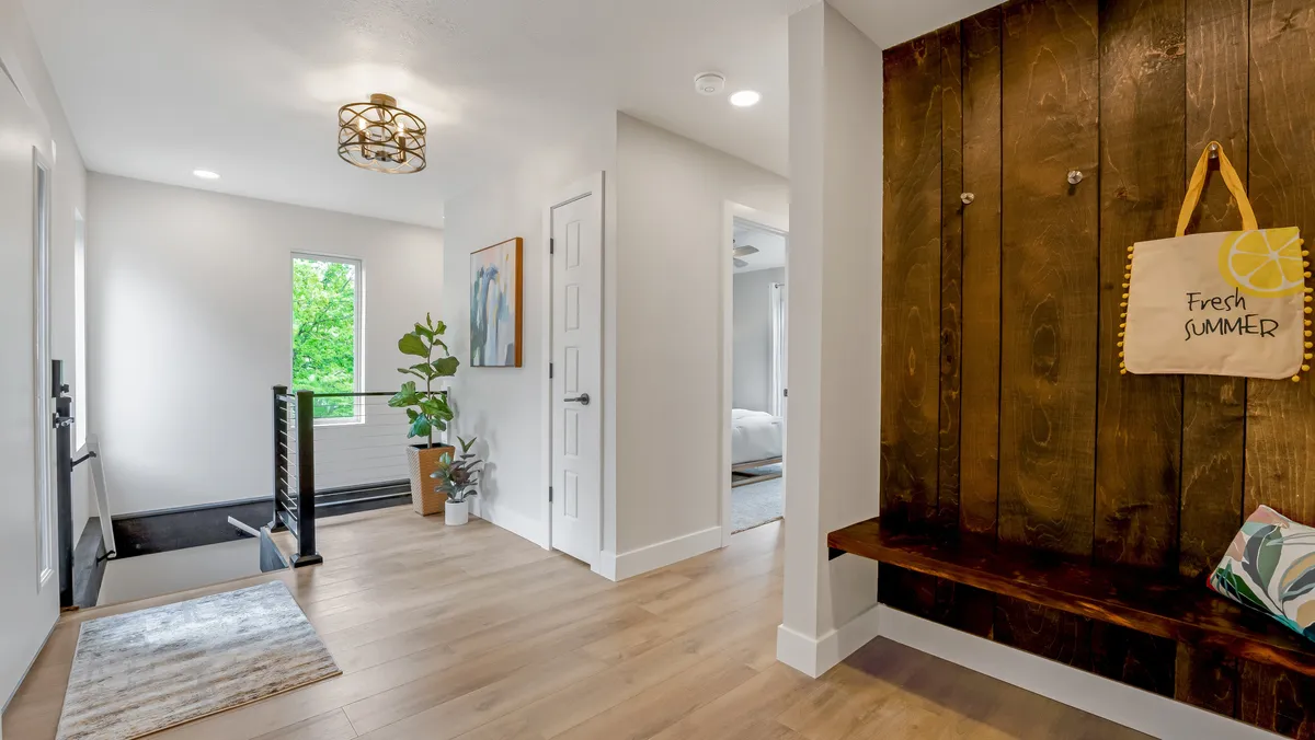 A charming entryway with a bench marked 'Fresh SUMMER,' a potted plant, vibrant artwork, and a staircase leading up. The area feels fresh, welcoming, and thoughtfully prepared for guests.