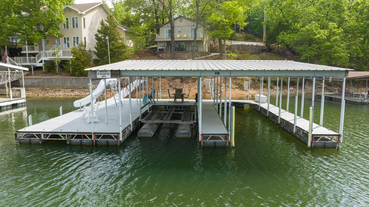 A lively exterior image featuring the dock with a waterslide and comfortable seating area. The dock extends over the water, inviting guests to swim, float, or launch paddleboards. The scene embodies playful lakeside fun and leisurely relaxation with sunset views in the background.