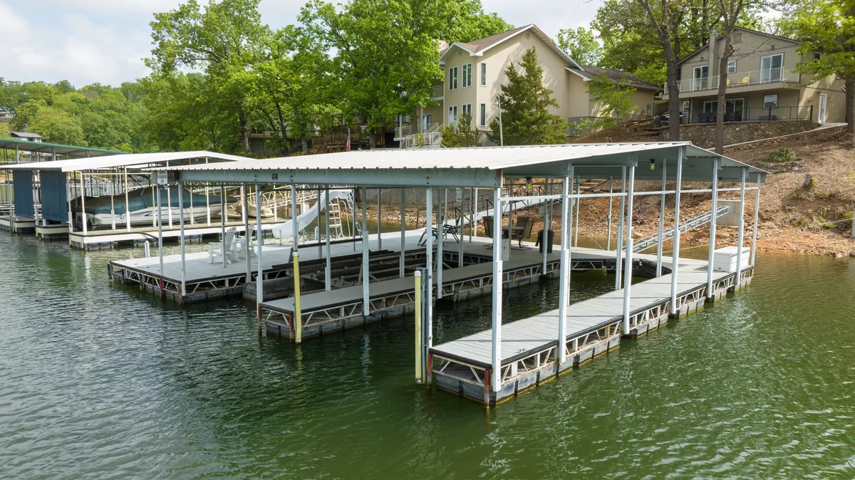 A serene lakeside scene featuring boat docks surrounded by lush greenery, calm water reflecting the sky, and space for fishing or relaxing by the water. The setting is peaceful yet clearly connected to the lake’s recreational opportunities.