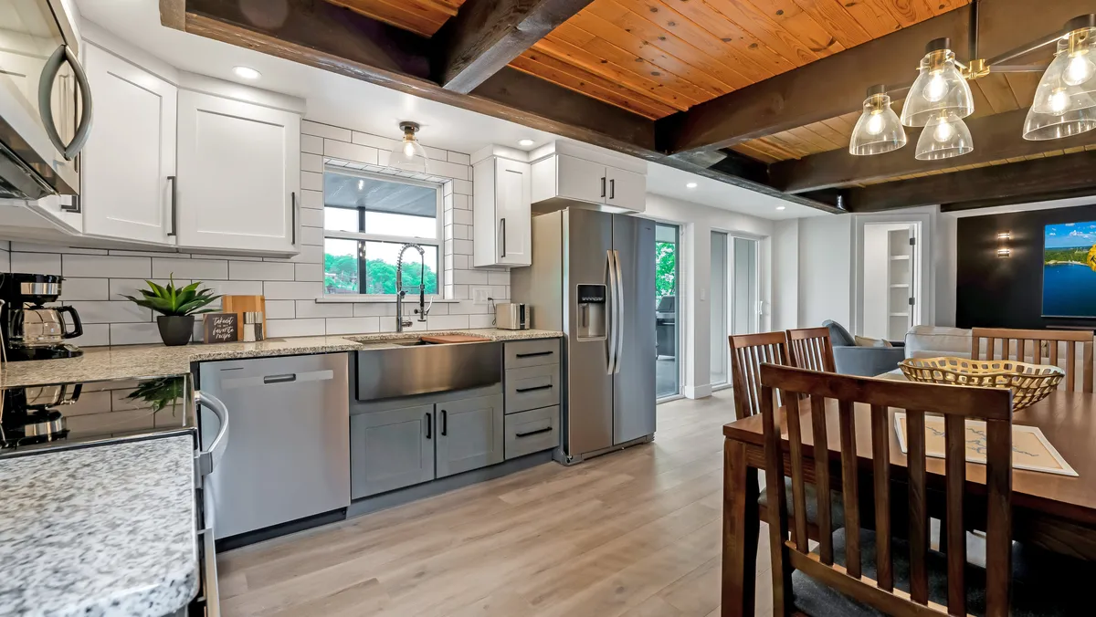 This scene highlights a kitchen with granite countertops, stainless steel appliances, a wooden dining table, and a large window that brings in natural light. The layout is inviting, perfect for cooking, family meals, and entertaining guests.