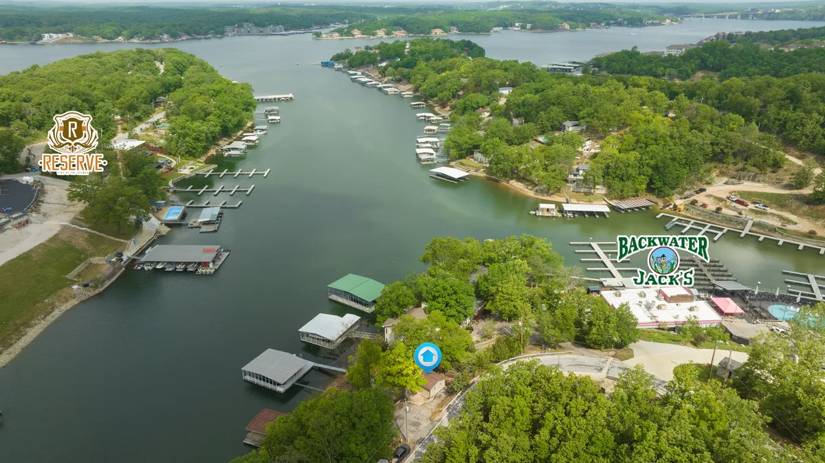A wide view overlooking the lake with visible marinas, green spaces, and lakefront restaurants. The image captures boats docked in the marina, tree-lined shores, and vibrant lakeside activity, suggesting easy access to dining and recreation.