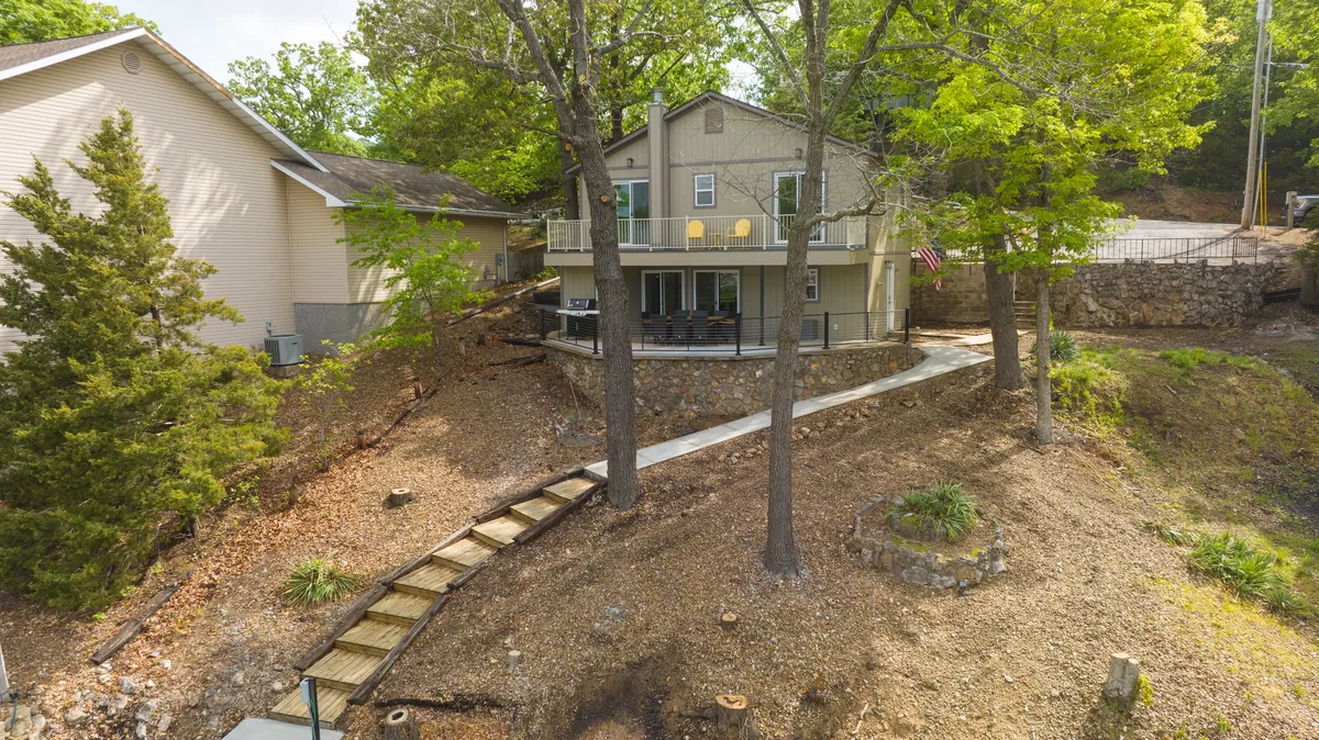 A welcoming exterior shot of the main house with a deck featuring yellow chairs, a pathway leading up to the entry, and the surrounding natural landscape. The image radiates tranquility and the potential for gatherings under the stars.