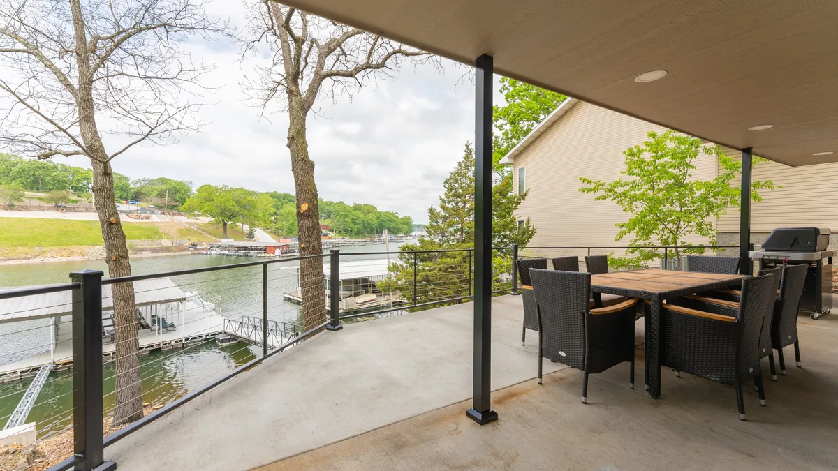 A tranquil exterior shot displaying an outdoor dining area on the deck, with a view of the water and surrounding trees. The dock is visible, illustrating direct access to the lake. The space is set up to enjoy morning coffee, evening barbecues, or group meals, all while immersed in natural beauty.