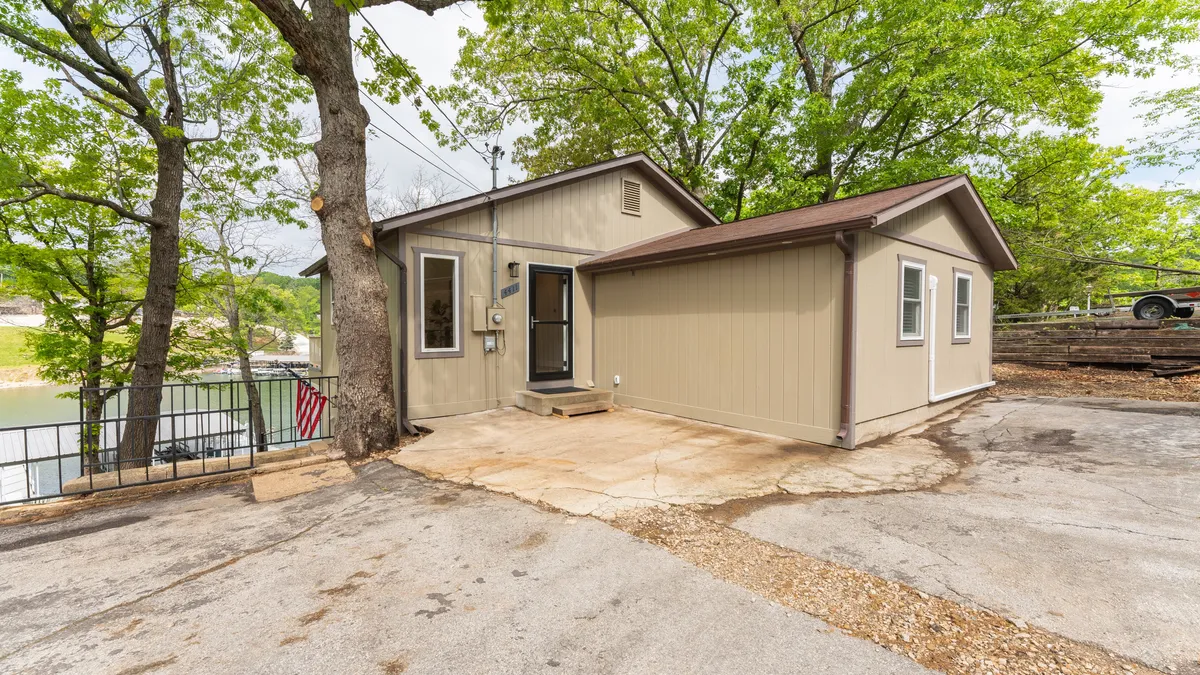 The image shows the front of the house under a tree canopy, with the driveway and entryway visible. The welcoming exterior suggests easy access for arrivals and a warm atmosphere for the whole family, pets included. The yard space also hints at areas where pets might play.