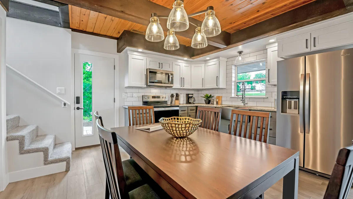 A warm, inviting dining area with a wooden table set for a family meal. The scene includes modern kitchen cabinetry and elegant lighting fixtures, conveying a sense of readiness and thoughtful provision for guests.